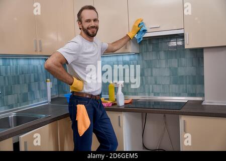 Junger kaukasischer Mann lächelt, während er Küchenmöbel putzt Stockfoto