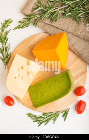 Grüner Basilikumkäse und verschiedene Käsesorten mit Rosmarin und Tomaten auf Holzbrett auf weißem Holzhintergrund. Draufsicht, Kopierbereich, selektiv Stockfoto