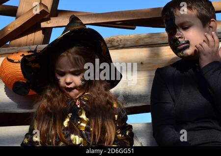 Kinder in halloween Kostümen im Urlaub ein Mädchen im Hexenanzug ein schwarzer Hut auf dem Kopf mit schwarzem Halloween Make-up, Junge im Teufel halloween Kostüm Stockfoto