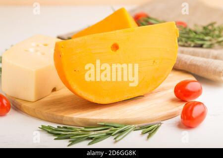 Verschiedene Käsesorten mit Rosmarin und Tomaten auf Holzbrett auf weißem Holzhintergrund und Leinentextilien. Seitenansicht, Nahaufnahme, selektiver Fokus Stockfoto