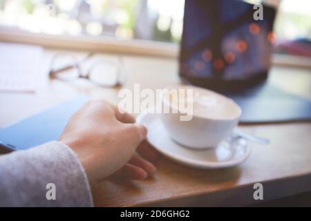 Nahaufnahme eines männlichen Freiberuflers oder Geschäftsmannes, der trinkt Kaffee Cappuccino während der Arbeit aus der Ferne im Café Stockfoto