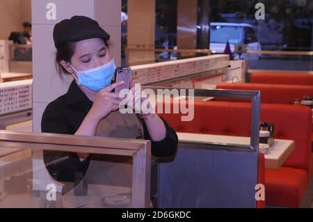 Eine kambodschanische Kellnerin, die eine schützende Gesichtsmaske trägt, macht während der COVID-19 Pandemie ein Foto mit einem Smartphone in einem leeren Restaurant. Phnom Penh, Kambodscha. © Kraig Lieb Stockfoto