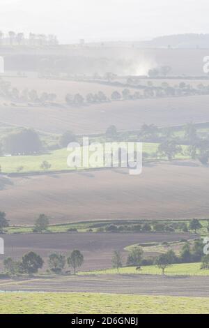 Traktoren pflügen Felder in der Ferne in einem Flickenteppich von landwirtschaftlichen Feldern in der englischen Landschaft in Northumberland Stockfoto