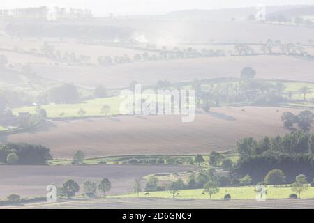 Traktoren pflügen Felder in der Ferne in einem Flickenteppich von landwirtschaftlichen Feldern in der englischen Landschaft in Northumberland Stockfoto