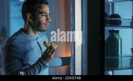 In der Nacht in der Küche Attraktive junge Mann isst eine übrig gebliebene Pizza aus dem Kühlschrank. Er ist hungrig und fühlt sich zufrieden. Stockfoto
