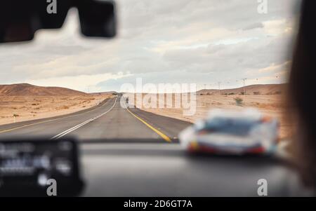 Autofahren durch Wüstenlandschaft an bewölktem Tag, Blick vom Beifahrersitz, verschwommenes Armaturenbrett im Vordergrund, Roadtrip-Konzept Stockfoto