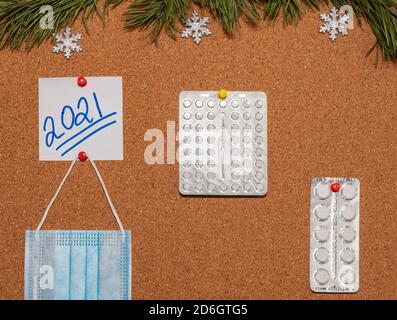 Medizinische Maske, weiße Pillen, weiße Haftnotiz mit 2021 auf Tafel, die mit Kiefernzweigen und Schneeflocken verziert ist. Gesundheitswesen, weihnachten Stockfoto