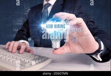 Geschäftsmann, der eine Glühbirne mit JETZT EINSTELLENDER Aufschrift hält, neues Geschäftskonzept Stockfoto