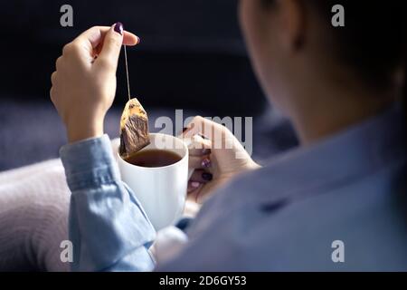 Frau hält Teebeutel in der Tasse, um ein gesundes heißes Getränk im Winter zu machen. Etwas warmes für die kalte Jahreszeit. Bio-Kräuter-Teebeutel. Friedliche Stimmung. Stockfoto