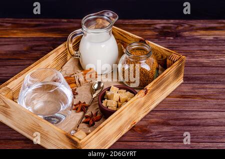 Zutaten für Dalgon-Kaffee in einer Schachtel auf einem Holzhintergrund. Instant-Kaffee, Anis, Zimt, Rohrzucker, Milch, Wasser. Platz kopieren, flach legen, Platz f Stockfoto