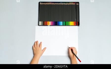 Kinderhand hält einen Bleistift zum Zeichnen. Buntstifte in einem Etui auf grauem Hintergrund.EIN Satz Bleistifte zum Zeichnen, Kreativität, Hobbys, Unterricht. Stockfoto