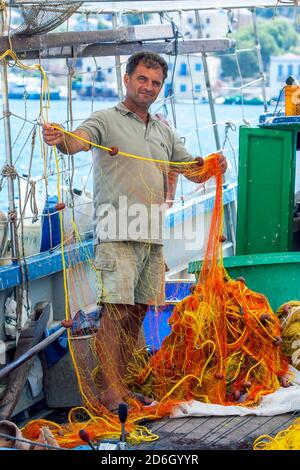 Ein Fischer an Bord eines Fischerbootes prüft seine Netze im Hafen der griechischen Insel Kastellorizo, auch bekannt als Meis-Insel. Stockfoto