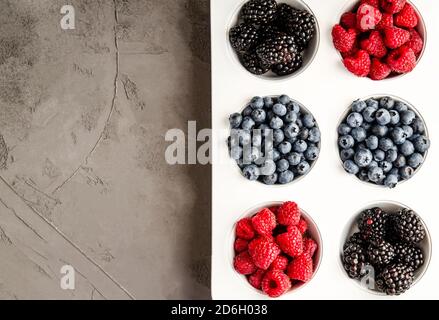 Frische Himbeeren, Blaubeeren und Brombeeren in einer weißen Eisenkalzform auf grauem Betongrund. Nahaufnahme, Platz kopieren, Saisonkonzept, Summe Stockfoto