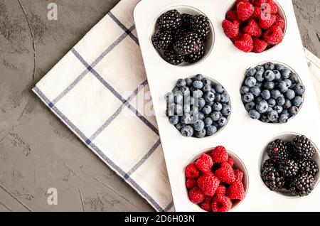 Frische Beeren Himbeeren, Heidelbeeren und Brombeeren im Weißeisenbacken, mit Serviette auf grauem Betongrund. Nahaufnahme, Platz kopieren, Saison Stockfoto