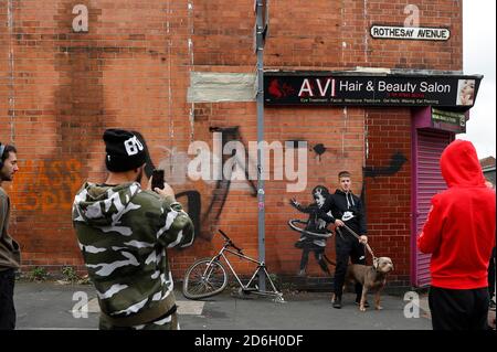 Nottingham, Nottinghamshire, Großbritannien. Oktober 2020. Ein Mann posiert mit seinem Hund neben einem Werk des Graffiti-Künstlers Banksy. Die Arbeit, außerhalb eines Schönheitssalons, zeigt ein Mädchen Hula-Hooping mit einem Fahrradreifen neben einem Fahrrad, das sein Hinterrad fehlt. Credit Darren Staples/Alamy Live News. Stockfoto