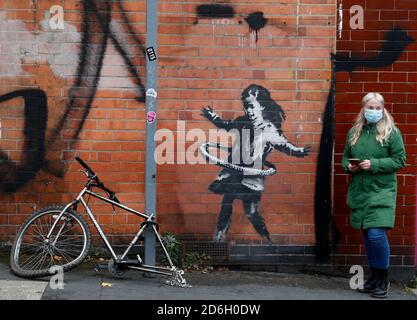 Nottingham, Nottinghamshire, Großbritannien. Oktober 2020. Eine Frau steht neben einem Werk der Graffiti-Künstlerin Banksy. Die Arbeit, außerhalb eines Schönheitssalons, zeigt ein Mädchen Hula-Hooping mit einem Fahrradreifen neben einem Fahrrad, das sein Hinterrad fehlt. Credit Darren Staples/Alamy Live News. Stockfoto