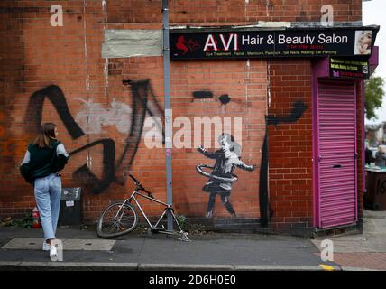 Nottingham, Nottinghamshire, Großbritannien. Oktober 2020. Eine Frau betrachtet ein Werk der Graffiti-Künstlerin Banksy. Die Arbeit, außerhalb eines Schönheitssalons, zeigt ein Mädchen Hula-Hooping mit einem Fahrradreifen neben einem Fahrrad, das sein Hinterrad fehlt. Credit Darren Staples/Alamy Live News. Stockfoto