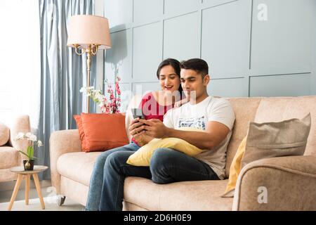 Indische asiatische junge Paar mit Smartphone zusammen während sitzen auf Sofa oder Couch und moderne Innenraum oder Zuhause Stockfoto