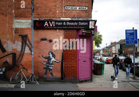 Nottingham, Nottinghamshire, Großbritannien. Oktober 2020. Ein Paar geht mit seinem Hund an einem Werk der Graffiti-Künstlerin Banksy vorbei. Die Arbeit, außerhalb eines Schönheitssalons, zeigt ein Mädchen Hula-Hooping mit einem Fahrradreifen neben einem Fahrrad, das sein Hinterrad fehlt. Credit Darren Staples/Alamy Live News. Stockfoto