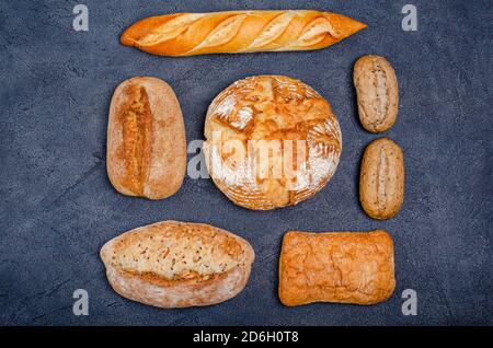 Bäckerei - verschiedene rustikale knusprige Brötchen mit Brot und Brötchen auf einem dunklen Hintergrund. Platz kopieren, flach legen, für Text platzieren. Blick von oben. Stockfoto