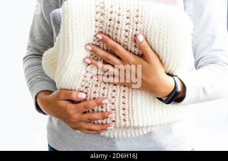 Weibliche Hände halten handgemachte Strickplaids aus hellem Naturgarn Nahaufnahme auf weißem Hintergrund. Die Atmosphäre des Winters, des Herbstes, mit dem Kopierraum, ho Stockfoto