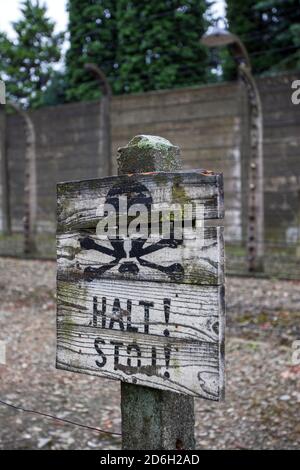 Ein Warnschild, das vor einem Stacheldraht-Elektrozaun im Staatlichen Museum Auschwitz-Birkenau in Polen angebracht ist. Stockfoto