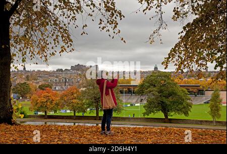 Inverleith Park, Edinburgh, Schottland, Großbritannien. 17. Oktober 2020. An einem bewölkten Tag verlieren die Bäume ihre Herbstfarben in Inverleith mit der Skyline der Innenstadt im Hintergrund. Eine Dame nimmt mit ihrem Handy einen Fotoaph. Quelle: Arch White/Alamy Live News Stockfoto