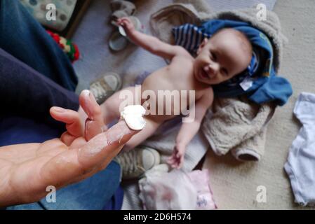 Vater Vater Vater Wickelwindel Wechsel hält Finger Sudocrem oben Ein glückliches lächelndes Baby, das auf dem Boden unter der Kleidung liegt In Wales Großbritannien KATHY DEWITT Stockfoto