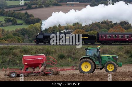 Die Dampflokomotive der S15-Klasse 506 passiert einen Traktor auf einem Feld, da sie sich entlang der Mid Hants Railway, auch bekannt als Watercress-Linie, in der Nähe von Ropley in Hampshire während der Herbst-Dampfgala am Wochenende befindet. Stockfoto