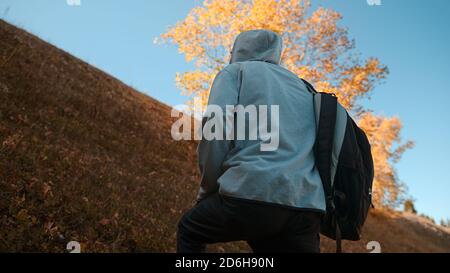 Hippie-Kletterer mit seinem Rucksack hinter ihm Klettern einen steilen Hang in den Wald, Natur und Lifestyle-Konzept Stockfoto