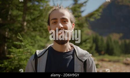 Naturalist lange Haare und bärtige Hipster Mann mit Rucksack Blick auf Kamera und lächelnd, Natur und Lifestyle-Konzept Stockfoto