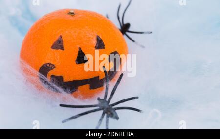 Leuchtend orange Halloween unheimlich Mandarine Emotion Gesicht auf weißem Spinnennetz Hintergrund mit Spinnen, selektiver Fokus. Stockfoto