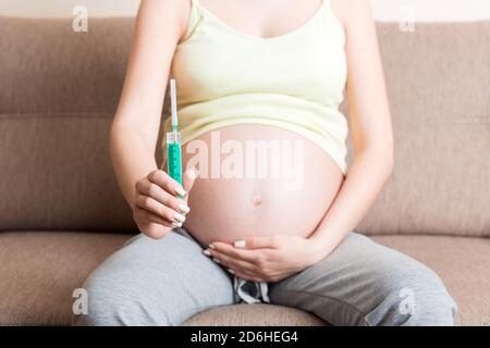 Spritze zur Injektion in die Hand der schwangeren Frau auf dem Sofa zu Hause, gesundes Millennial Healthcare-Konzept. Stockfoto