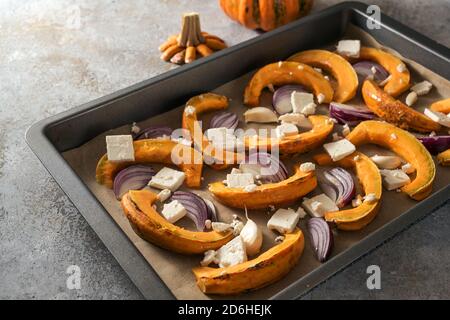 Rohe Kürbis- oder Squashscheiben auf einem Backblech mit roten Zwiebeln, Knoblauch und Feta-Käse, Kochen mit Herbstgemüse für Thanksgiving und Halloween Stockfoto