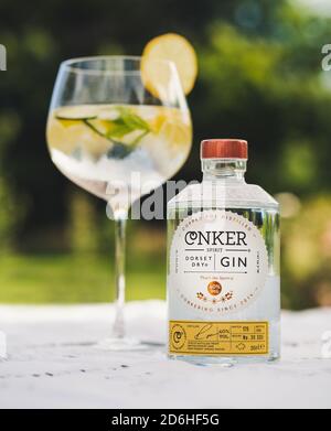 Großes Glas Gin und Tonic Drinks mit Eis und Zitrone mit Conker Dorset Dry Gin Flasche mit Lavendelbüschen im Sommersonnenlicht auf weißem Tisch Stockfoto