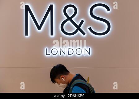 Ein Fußgänger mit Gesichtsmaske geht am britischen multinationalen Einzelhändler Mark & Spencer (M&S) und seinem Logo in Hongkong vorbei. Stockfoto