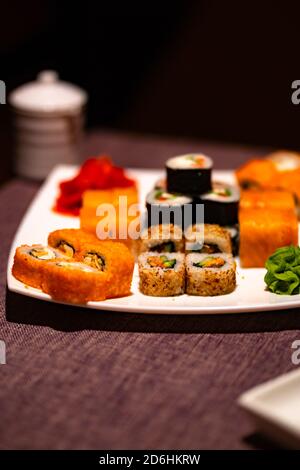 Serviert appetitliches Sushi auf weißem Teller im Café. Nahaufnahme von leckeren Sushi-Brötchen mit Wasabi und Ingwer im traditionellen japanischen Restaurant. Stockfoto