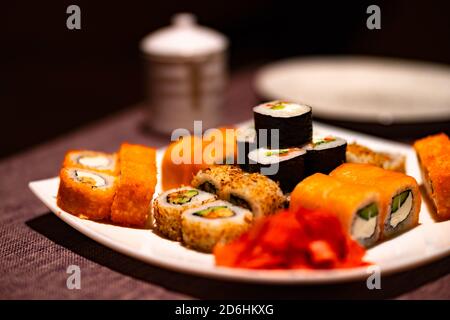 Serviert appetitliches Sushi auf weißem Teller im Café. Nahaufnahme von leckeren Sushi-Brötchen mit Wasabi und Ingwer im traditionellen japanischen Restaurant. Stockfoto