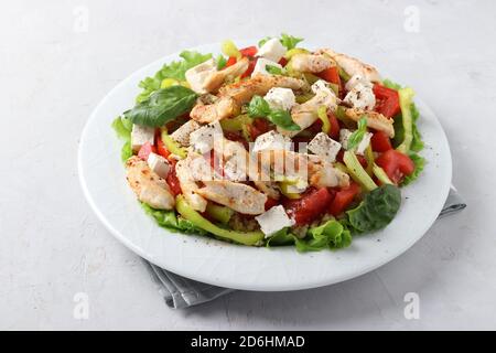 Salat mit Bulgur, gebackenem Huhn, Paprika, Basilikum und Feta auf einem weißen Teller, Closeup Stockfoto