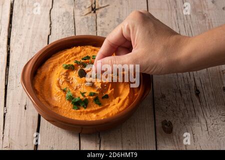 Frau bereitet Kürbis Hummus in Schüssel auf Holztisch Stockfoto