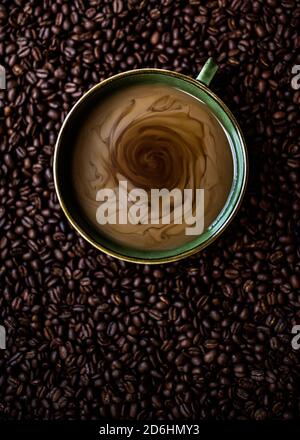 Grüner Becher aus wirbelndem Kaffee und Milch, umgeben von gerösteten Kaffeebohnen Stockfoto