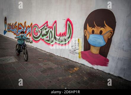 Gaza, Palästina. Oktober 2020. Ein palästinensischer Junge fährt mit dem Fahrrad an einem Wandgemälde vorbei, auf dem ein Kind mit einer Maske an einer Wand in Khan Yunis im Süden des Gazastreifens abgebildet ist. Kredit: Yousef Masoud/SOPA Images/ZUMA Wire/Alamy Live Nachrichten Stockfoto