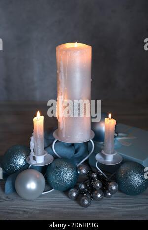 Brennende Kerzen mit Weihnachtsschmuck und einer Geschenkbox auf einem Holzhintergrund. Stockfoto