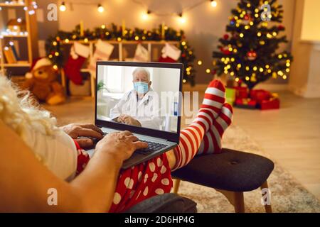 Der Weihnachtsmann hört einem Arzt in einer schützenden medizinischen Maske mit einem Videoanruf zu. Stockfoto