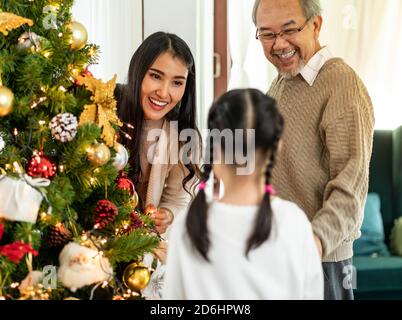 Mehrgenerationenübergreifende asiatische Familie, die einen Weihnachtsbaum schmückt. Mama Tochter Mädchen und Großvater schmücken den Weihnachtsbaum Vorbereitung für die Saison Gruß Stockfoto