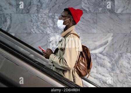 Afro-amerikanischer Reisender Mann steht auf Rolltreppe in U-Bahn oder Bahnhof, tragen Gesicht medizinische Maske, um sich vor Kontakt mit Grippe-Virus zu schützen, p Stockfoto