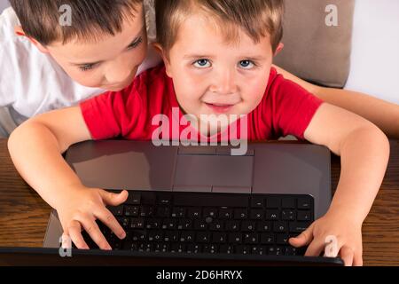 Ein 4-jähriges Kleinkind hat Spaß auf einem Laptop-Computer, Blick auf die Kamera, während sein älterer Bruder wacht über seine Schulter. High-Angle-Ansicht Isolat Stockfoto