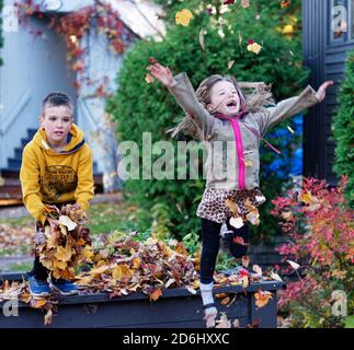 Zwei Kinder, ein 8-jähriger Junge und seine 6-jährige Schwester, springen und werfen mit Herbstblättern spielen Stockfoto