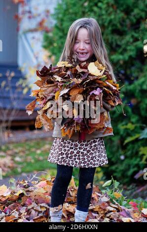 Ein lächelndes 6-jähriges Mädchen, das ein Bündel hält Herbstlaub Stockfoto