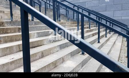 Externe mehrstufige Steintreppe. Es gibt viele Treppen und Geländer aus Metall. Viele Schritte in einer städtischen Umgebung, symbolisch abstrakt zurück Stockfoto